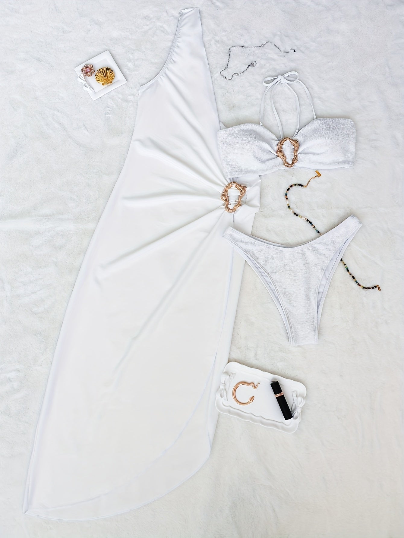 Conjunto biquíni feminino um ombro só branco com saia pareô em flat lay sobre superfície tipo cama