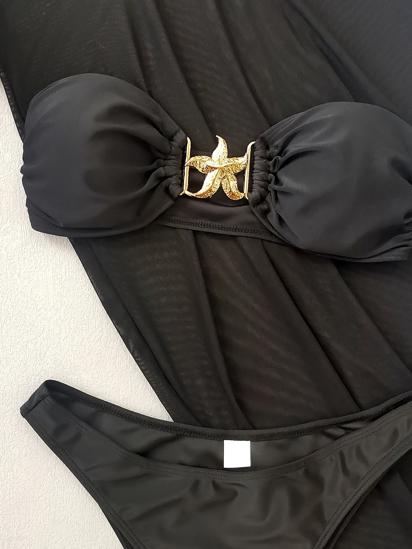 Detalhe do top do biquíni preto com estrela dourada e acabamento premium
